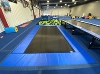 Indoor trampoline park with blue trampolines and basketball hoop.